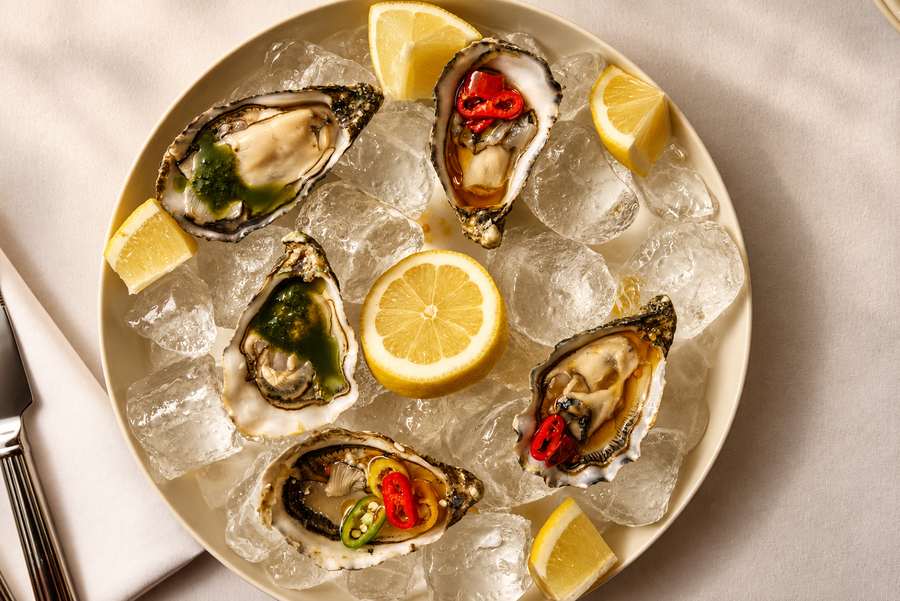 Five oysters on ice with lemon wedges and a lemon half in the centre