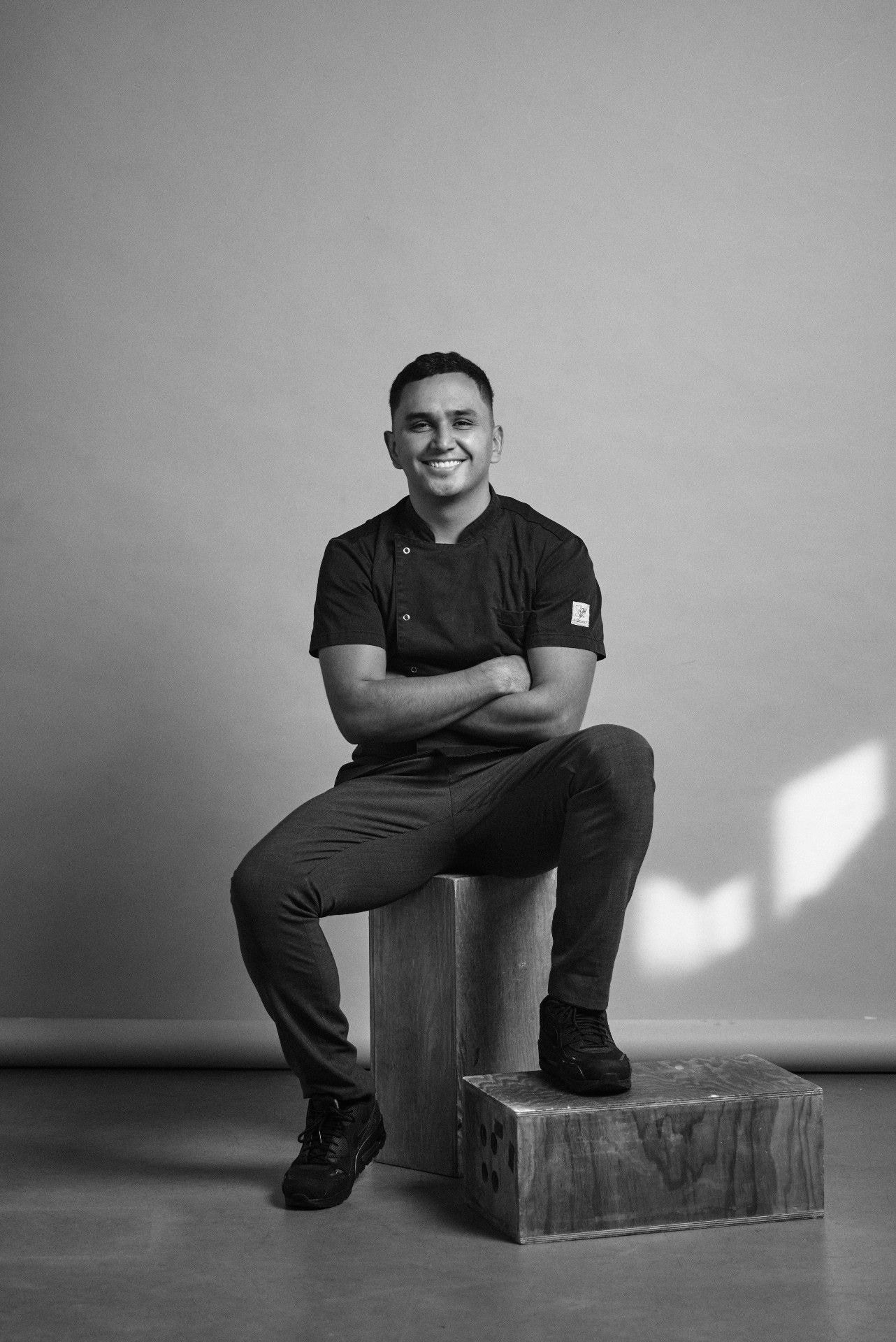 Portrait of host Julián Castro seated in a kitchen jacket, black and white